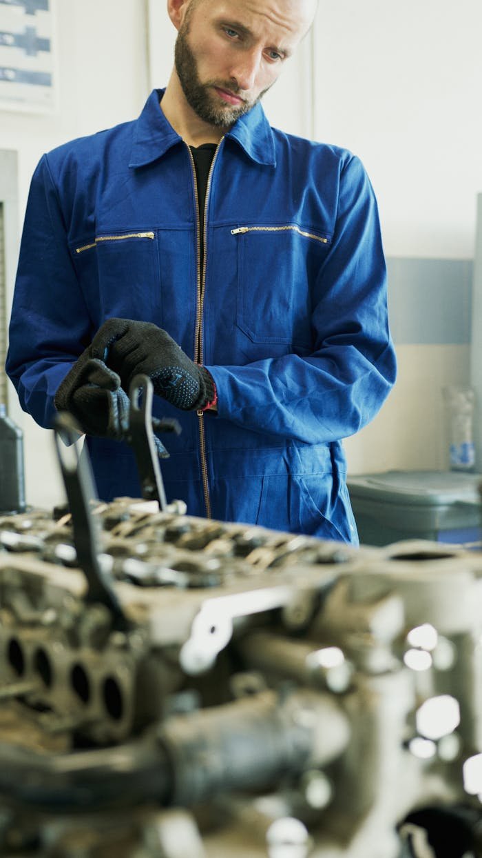A Man in Blue Coveralls Repairing an Engine